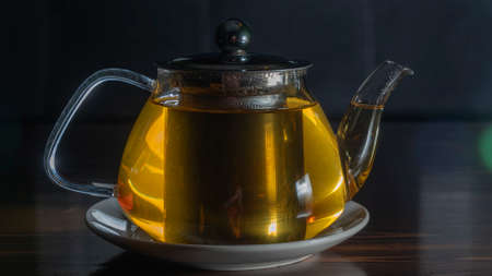 Glass teapot with tea on dark background. Green tea and teapot on wooden table. advertising composition. Space for text.の写真素材