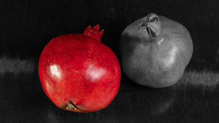 Whole red pomegranate and black and white pomegranate on wooden background. Fresh raw organic garnet fruit. Garnet is a symbol of Judaism, fertility, abundance and marriage. selective focus.の写真素材
