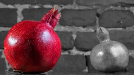 Whole red pomegranate and black and white pomegranate on brick wall background. Fresh raw organic garnet fruit. Pomegranate is a symbol of Judaism, fertility, abundance and marriage. Allegory sign.の写真素材