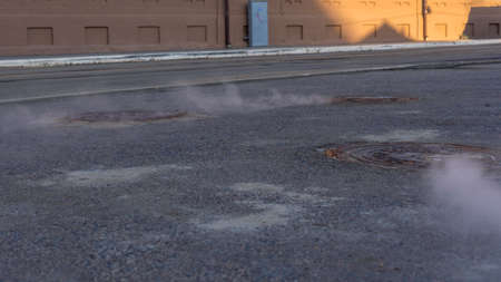 Manhole cover in a paved street on a cold day, as steam escapes from the sewer below up into the city street. Heavy steam coming out of a city center sewer.の写真素材