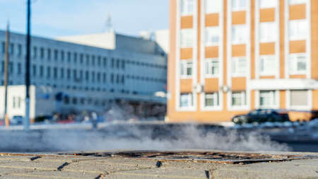 Manhole cover in a paved street on a cold day, as steam escapes from the sewer below up into the city street.の写真素材