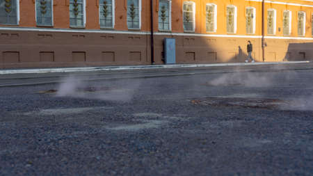 Manhole cover in a paved street on a cold day, as steam escapes from the sewer below up into the city street. Heavy steam coming out of a city center sewer.の写真素材