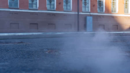 Manhole cover in a paved street on a cold day, as steam escapes from the sewer below up into the city street. Heavy steam coming out of a city center sewer.の写真素材