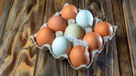 Close-up view of raw chicken eggs with feather in egg box on wooden background. Chicken eggs in...
