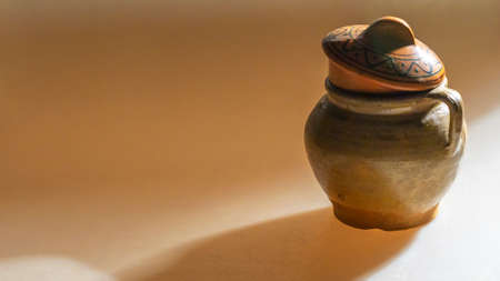 A clay pot in deep shadows on a uniform yellow background. Vintage clay pot for cooking. One ceramic...