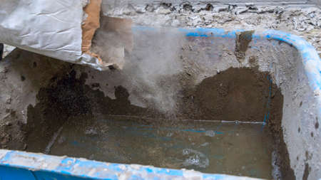 Construction worker pouring the cement to the bucket. Adhesive mixing. Waiting to be mixed with cement. Construction workers or technicians is mixing the cement in the bucket.の写真素材