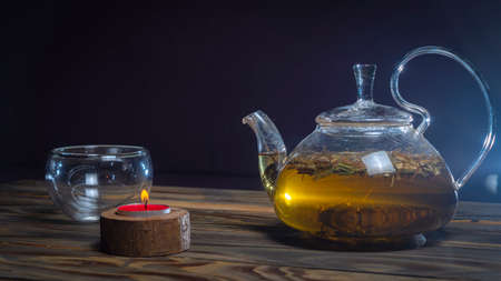 Hot herbal tea in glass teapot on wooden table on dark background. traditional herbal drink. Place...
