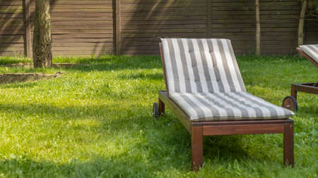 Lounge chair on the backyard in a beautiful garden. Empty sunbed on the grass. Concepts of recreation, tanning in the yard.の写真素材
