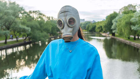 A girl in a gas mask stands on a bridge across the river. alienation in the city. Fashion, ecology and loneliness concepts. Coronavirus. ecological and epidemic problems.の写真素材