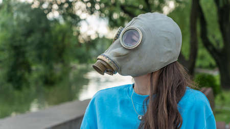 Girl with long hair in a gas mask on the river bank. alienation in the city. Fashion, ecology and loneliness concepts. Coronavirus. ecological and epidemic problems.の写真素材