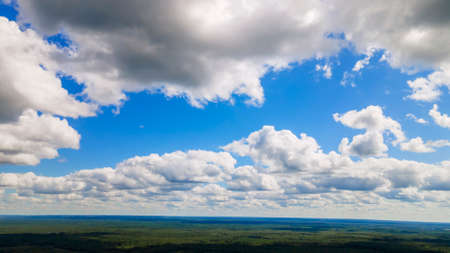 Blue sky panorama with clouds over tops of green trees. Blue sky and white cloud soft. White cloud background. Green tree top line over blue sky and clouds background in summer.の写真素材