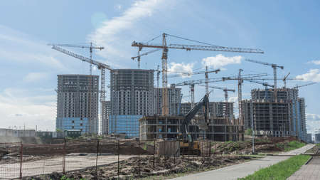 Construction of a multi-story residential buildings. Defocused foreground with young tree. Cranes work. construction site. Big development construction. Sunny summer day.の写真素材