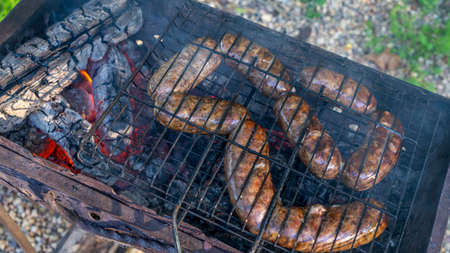 Tasty homemade sausage made of beaver meat cooking on grill. Beaver meat sausages are cooked on coals. Homemade beaver sausages.の写真素材