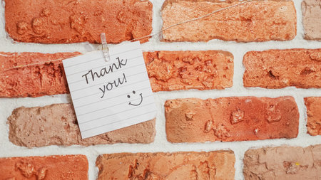 A colorful note saying "Thank you" with a smiley face is pinned to a rustic brick wall, conveying a cheerful message of gratitude and positivity in an urban setting.の写真素材