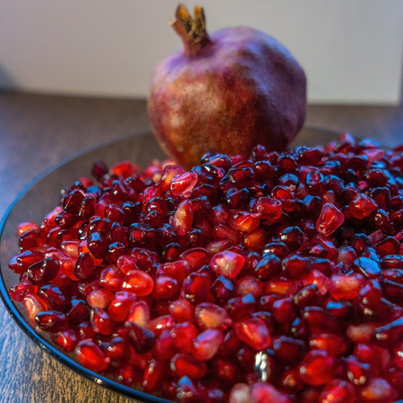 A bowl filled with vibrant, peeled pomegranate seeds alongside a whole pomegranate. The juicy arils glisten, showcasing their rich color and texture, perfect for healthy snacks or recipes.の写真素材