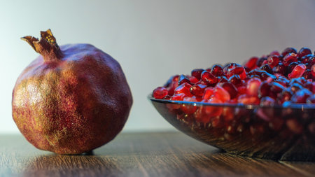 A bowl filled with vibrant, peeled pomegranate seeds alongside a whole pomegranate. The juicy arils glisten, showcasing their rich color and texture, perfect for healthy snacks or recipes.の写真素材