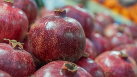 A vibrant close-up of a pomegranate at a bustling market, showcasing its rich red color and textured skin. The blurred background hints at a lively marketplace, emphasizing the fruit's freshness and appeal.の写真素材