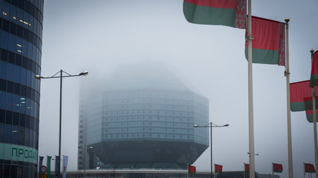 A modern building of the National Library of Belarus emerges from the fog, showcasing its futuristic glass design and adorned with Belarusian flags, creating a captivating atmosphere.の写真素材