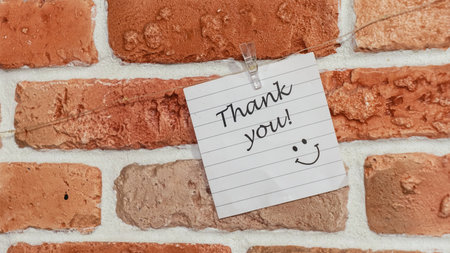 A colorful note saying "Thank you" with a smiley face is pinned to a rustic brick wall, conveying a cheerful message of gratitude and positivity in an urban setting.の写真素材