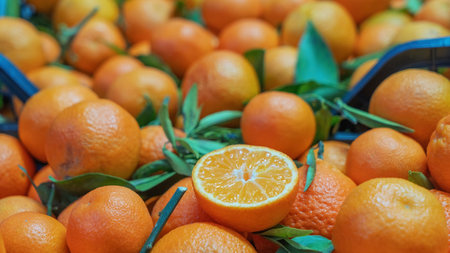 A vibrant market scene featuring a pile of fresh mandarins, with one mandarin cut in half, showcasing its juicy interior. The colorful display highlights the appeal of this delicious citrus fruit.の写真素材
