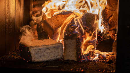 Eco-friendly compressed wood briquettes ignite a warm, inviting fire in a modern stove, showcasing sustainable heating and cozy ambiance for any homeの写真素材