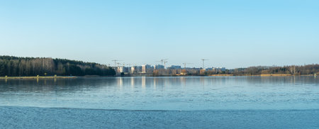 A modern residential area by a water body in the city, showcasing new home construction and the demolition of older structures. The urban landscape reflects the transition of winter into spring.の写真素材