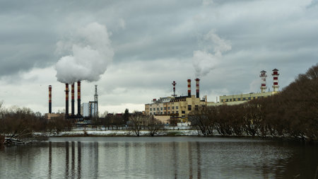 Industrial chimneys emit thick smoke into the winter sky, highlighting urban air pollution. A lakeside power plant symbolizes energy production, environmental challenges, and urbanization.の写真素材