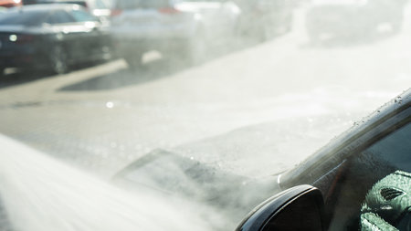 A self-service car wash featuring a high-pressure water spray cleaning a vehicle. Active foam covers...