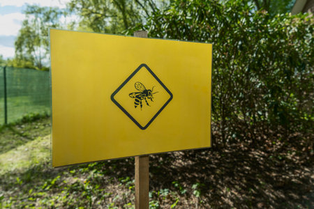 Warning bees - yellow sign featuring a bee in front of the beehive. Caution bees - homemade sign with a bee image in front of the apiary.の写真素材