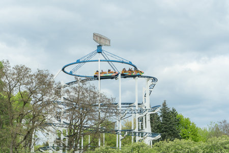 Thrilling Amusement Park Ride Soaring Above Lush Green Trees Under A Bright Sky. Exciting Adventure Ride At A Colorful Amusement Park With A Clear Blue Sky.の写真素材
