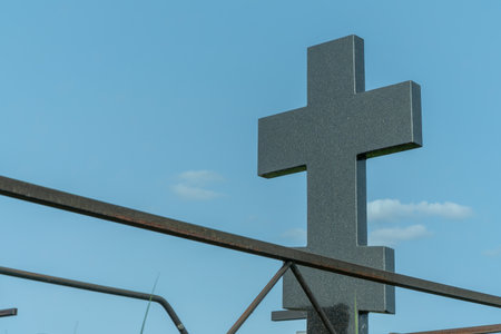 Marble cross in a serene cemetery. In the embrace of nature a granite cross stands as a testament to love and loss surrounded by vibrant flowers whispering stories of the past.の写真素材
