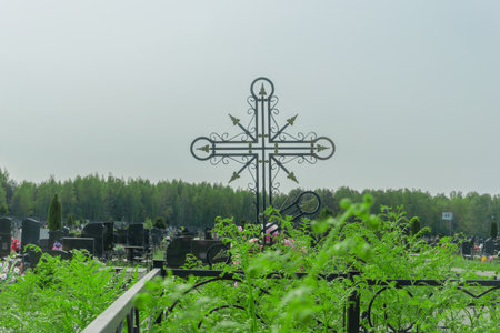 Ornate iron cross in a serene cemetery setting. A black metal cross amidst vibrant ferns represents the juxtaposition of mourning and the vibrant life that continues to thrive in the face of loss.の写真素材