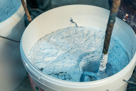 Production of decorative plaster at the factory. Materials for repair and decoration. Closeup of blue decorative plaster mixture in a bowl showcasing texture and contrast.の写真素材