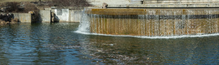An artificial waterfall on a city canal creates a stunning blend of urban design and natural beauty. Water cascades gracefully, adding motion and serenity to the urban landscape.の写真素材