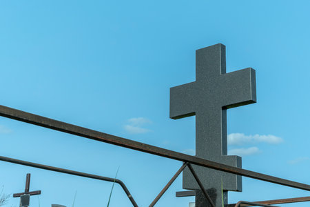 Marble cross in a serene cemetery. In the embrace of nature a granite cross stands as a testament to...