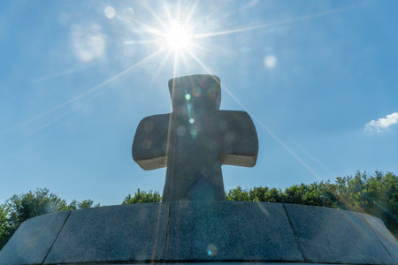 A solitary stone cross on a hill bathed in sunlight represents the enduring spirit of sacrifice and...