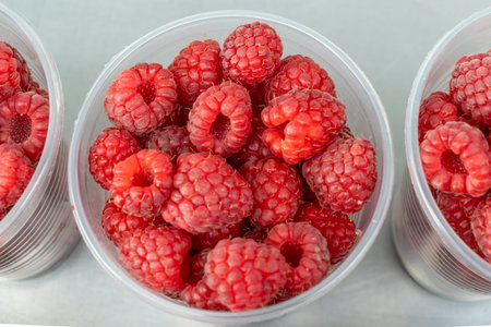 Freshly picked raspberries in clear cups at the market. Delightful moments captured with luscious...