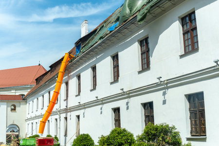 Historic buildings require careful renovation, building debris travels through an orange chute during roof repairs. Renovation of an old building. The roof is under construction.の写真素材