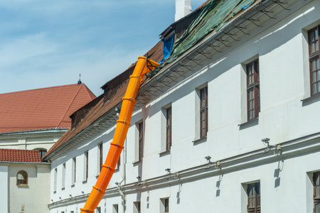 Historic buildings require careful renovation, building debris travels through an orange chute during roof repairs. Renovation of an old building. The roof is under construction.の写真素材