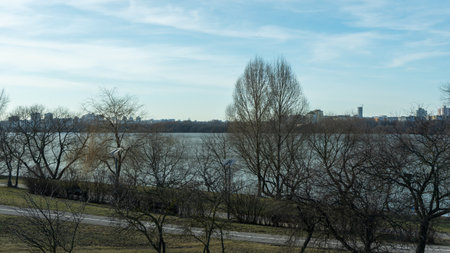 Urban waterfront park with paved walkway bare trees and street lamps overlooking midrise buildings...