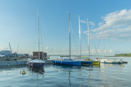 Sailboats docked at quiet marina under clear blue sky. Yachts moored quietly in the harbor, poised...