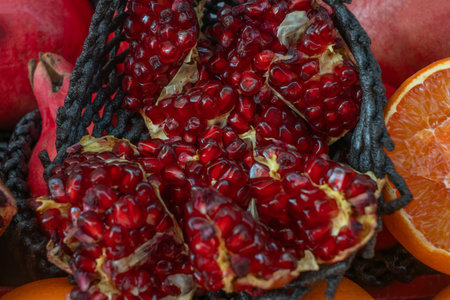 Open pomegranate with red seeds surrounded by whole fruits and orange slice. Pomegranates in rustic basket showcasing vibrant colors juicy textures and organic produce for culinary.の写真素材