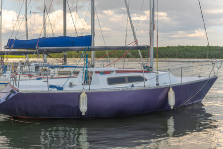 Peaceful marina with sailboats moored on tranquil lake under dramatic clouds and mirrored reflections in nature. Sailboats docked on calm water with reflections and cloudy sky.の写真素材