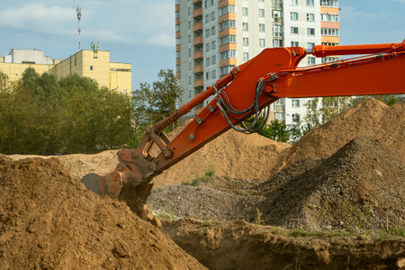 Excavator digging soil on construction site with urban buildings in the background. Industrial excavator performing earthmoving operations at construction site for residential infrastructure.の写真素材