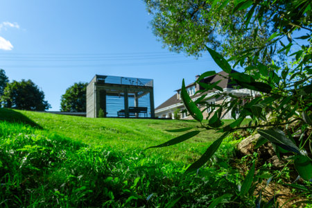 Residential house with porch lawn and wooden structures under clear blue sky. Well maintained countryside home with porch carport and wooden annex ideal for real estate architecture lifestyle.の写真素材