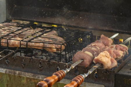 Grilled sausages cooking over hot charcoal on outdoor barbecue. Outdoor grilling of fresh sausages on charcoal barbecue with smoke heat and summer garden background.の写真素材