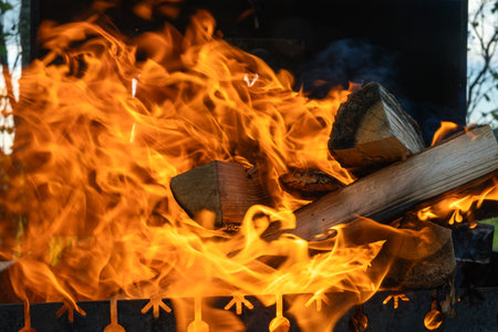 Campfire flames burning wood in outdoor metal grill. Primitive warmth and elemental energy of fire captured in outdoor grill with burning wood and nature in early transition.の写真素材