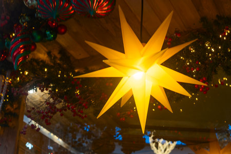 Illuminated yellow star ornaments and holiday garlands with berries and baubles. Glowing star shaped decorations with festive garlands and colorful ornaments in cozy rustic interior.の写真素材