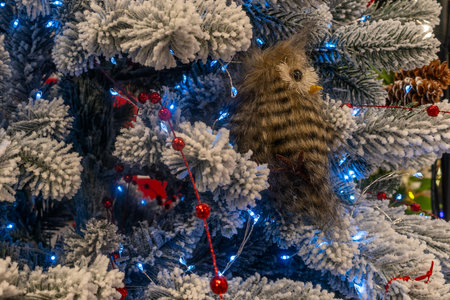 Christmas tree with plush owl ornament and blue lights. Closeup of snow covered christmas tree with glowing blue lights red beads and soft owl decoration nestled in branches.の写真素材