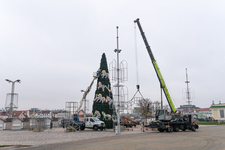Workers assembling a large artificial christmas tree in urban square. Urban holiday preparations with cranes and lifts decorating monumental artificial Christmas tree in public square.の写真素材